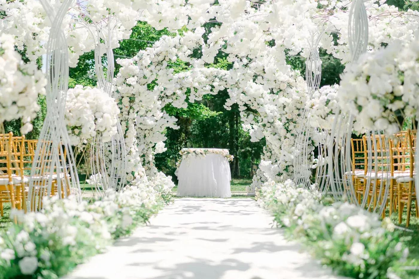 An outdoor wedding aisle framed by white floral arches.
